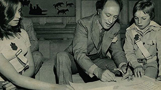 Photo en noir et blanc de l’ancien premier ministre Pierre Elliott Trudeau signant un document en compagnie de deux brigadiers portant leur ceinture.