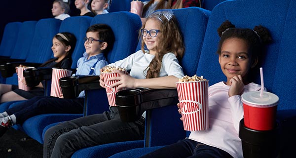 Image showing a group of young kids in a movie theatre watching the screen and smiling while holding boxes of popcorn.