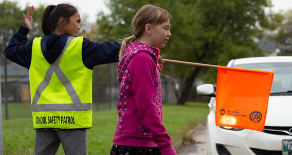 Image showing a student crossing a street behind a school patroller stopping traffic with her orange flag.