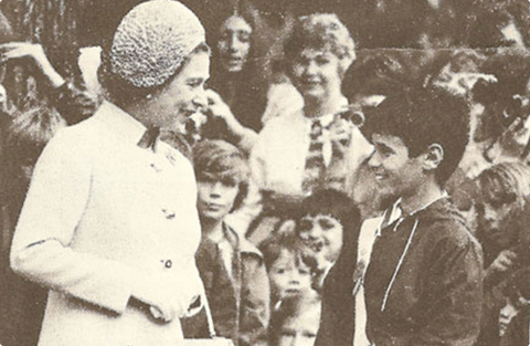 Black and white photo of student Paul Attard, wearing his School Safety Patrol belt, interacting with Queen Elizabeth II in London Ontario, 1973.