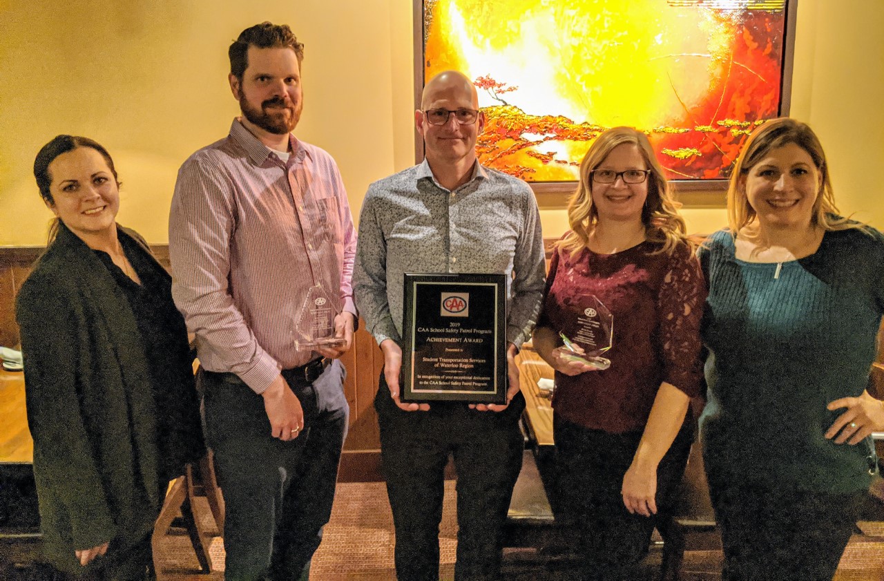 Three members of the Student Transportation Services of Waterloo Region team, along with two CAA representatives, pose with their 2019 Program Achievement (Community) Award.